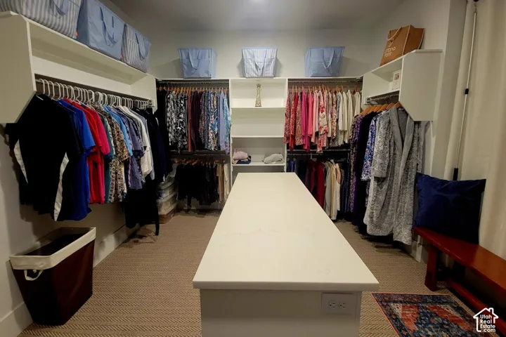 Spacious walk-in closet featuring extensive built-in shelving, multiple hanging rods, and a central island with a solid surface countertop