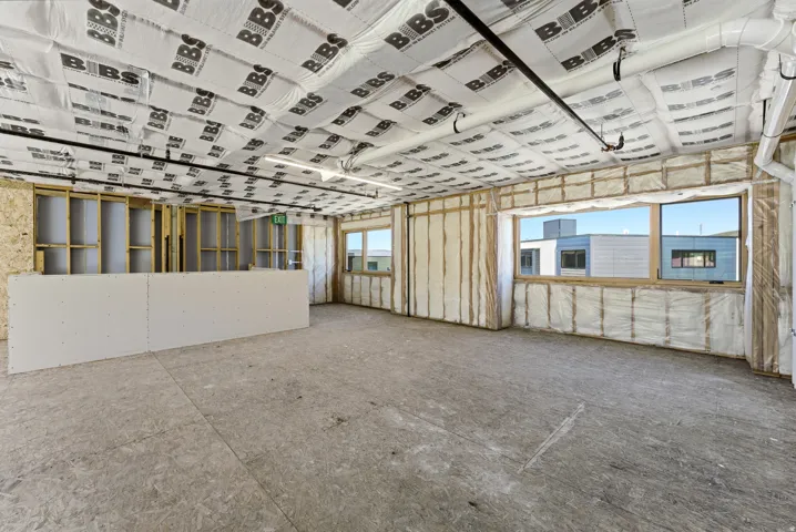 Open-concept space featuring exposed ceiling joists with insulation, a partial drywall partition, and two large windows