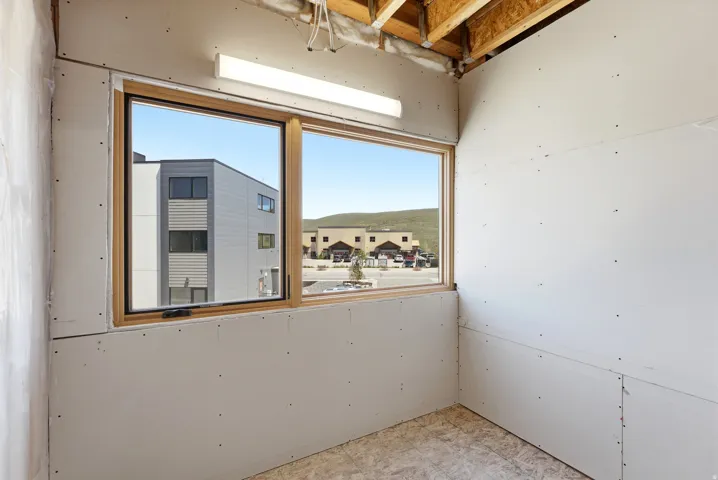 Room under construction featuring drywall installation, unfinished wood-finish flooring, and exposed ceiling joists