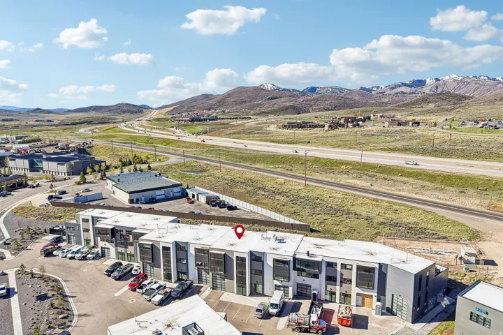Modern commercial building with a grey and white facade, multiple roll-up garage doors, ample on-site parking, and immediate proximity to a major highway