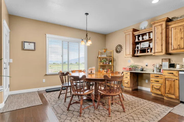 Dining area featuring wood-finish flooring, a large window with horizontal blinds, built-in wooden cabinetry with open shelving, and a granite-look countertop