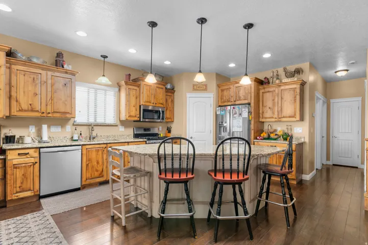 Kitchen featuring a central island with a built-in breakfast bar, granite countertops, wood-finish cabinetry, stainless steel appliances, and wood-finish flooring