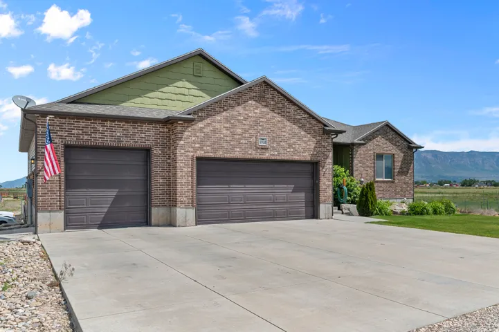 Brick facade residence featuring a two-car garage with panel doors, a concrete driveway, and a pitched roofline