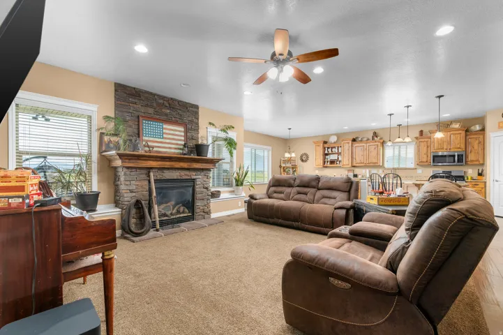 Living area featuring a stone-faced fireplace with a wood mantle, recessed lighting, and a ceiling fan