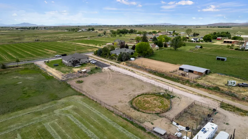 Expansive property featuring a contemporary residence with a multi-level deck, a round pen, multiple fenced enclosures, a barn structure, and surrounding agricultural fields