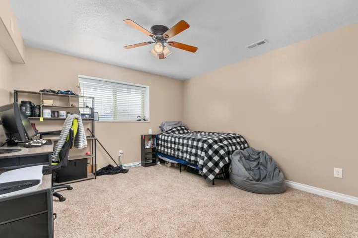 Carpeted room featuring a single window with blinds, a ceiling fan with light fixture, neutral wall paint, and white trim