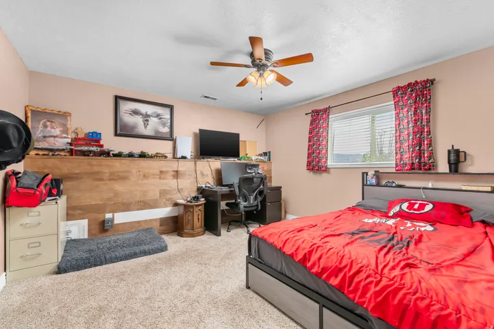 Carpeted room featuring a ceiling fan with light kit, a window with blinds, and a built-in wood-finish accent wall