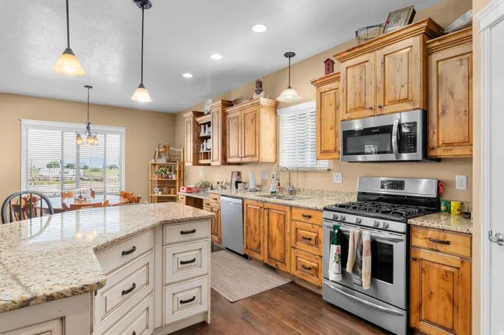 Open-concept kitchen featuring wood-finish cabinetry, granite-style countertops, stainless steel appliances, and a central island with white wood-finish cabinetry and pendant lighting