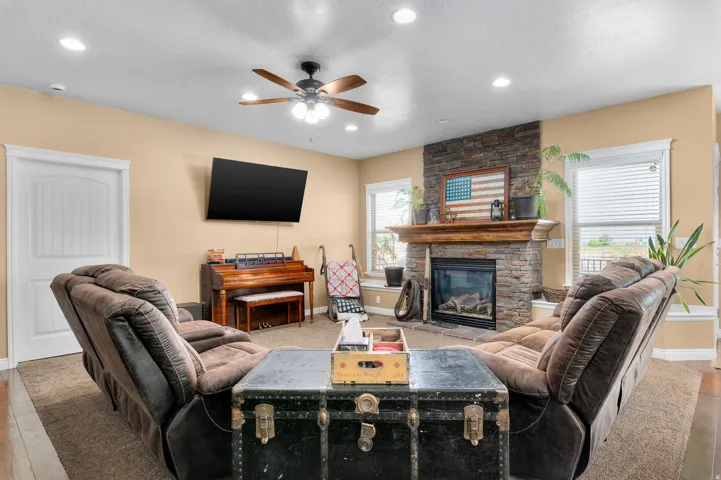 Living area featuring a stone-clad fireplace with a wood mantel, a ceiling fan with integrated lighting, recessed lighting, and wood-finish flooring
