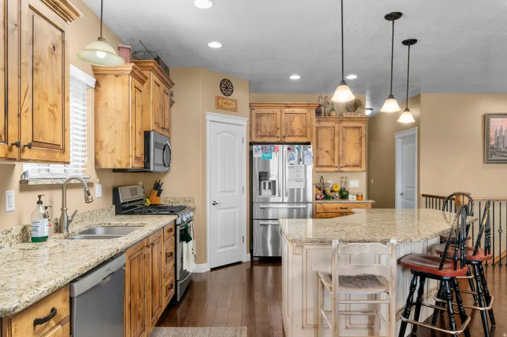 Kitchen featuring wood-finish cabinetry, granite countertops, stainless steel appliances, a kitchen island with pendant lighting, and dark wood-finish flooring