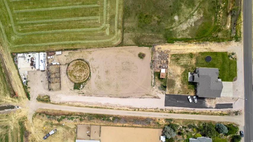 Expansive property featuring a large residence with a dark gray roof, a circular dirt arena, multiple outbuildings, a paved driveway, and substantial undeveloped land