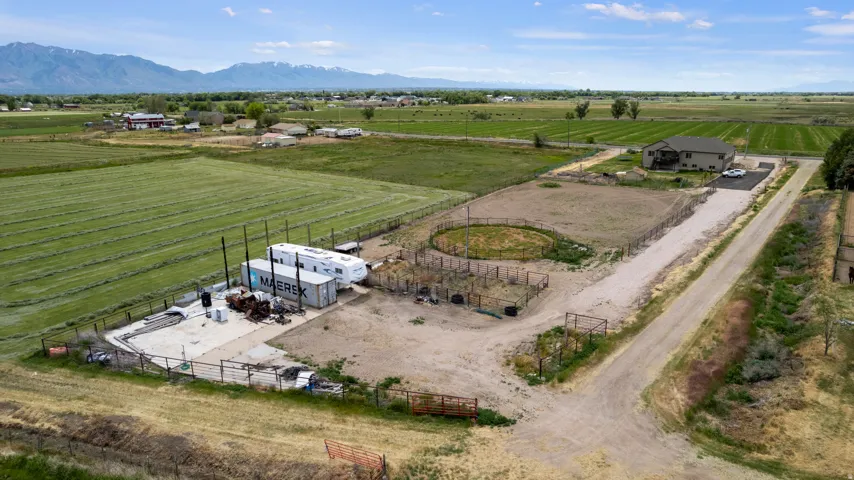 Expansive rural property featuring a multi-level residence with an attached garage, a circular fenced animal enclosure, a large gravel driveway, and surrounding agricultural fields