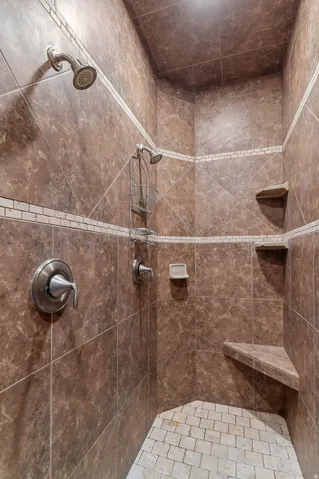 Tiled shower enclosure featuring dual shower heads, a built-in corner bench, and integrated corner shelving