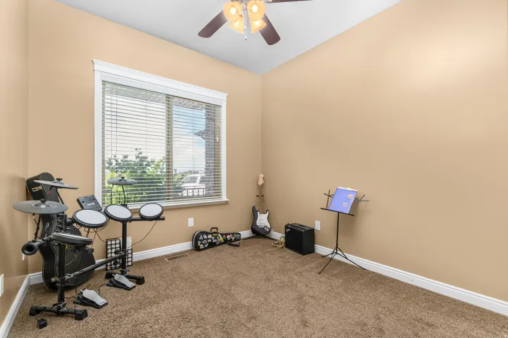 Carpeted interior room featuring a large window with horizontal blinds, a ceiling fan with integrated lighting, and crown molding