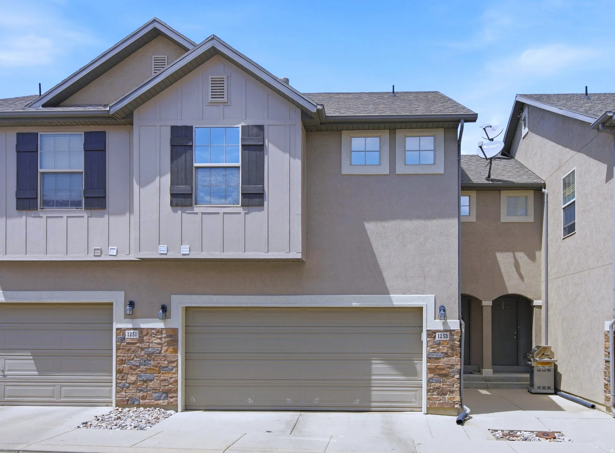 Contemporary stucco exterior featuring a stone accent façade, attached garage with a paved driveway, and gabled rooflines