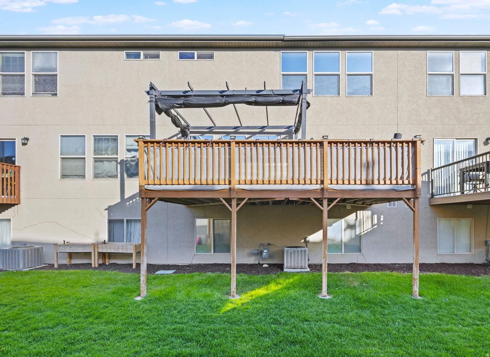 Rear exterior featuring a spacious elevated deck with wood railings, a ground-level patio, and a manicured lawn