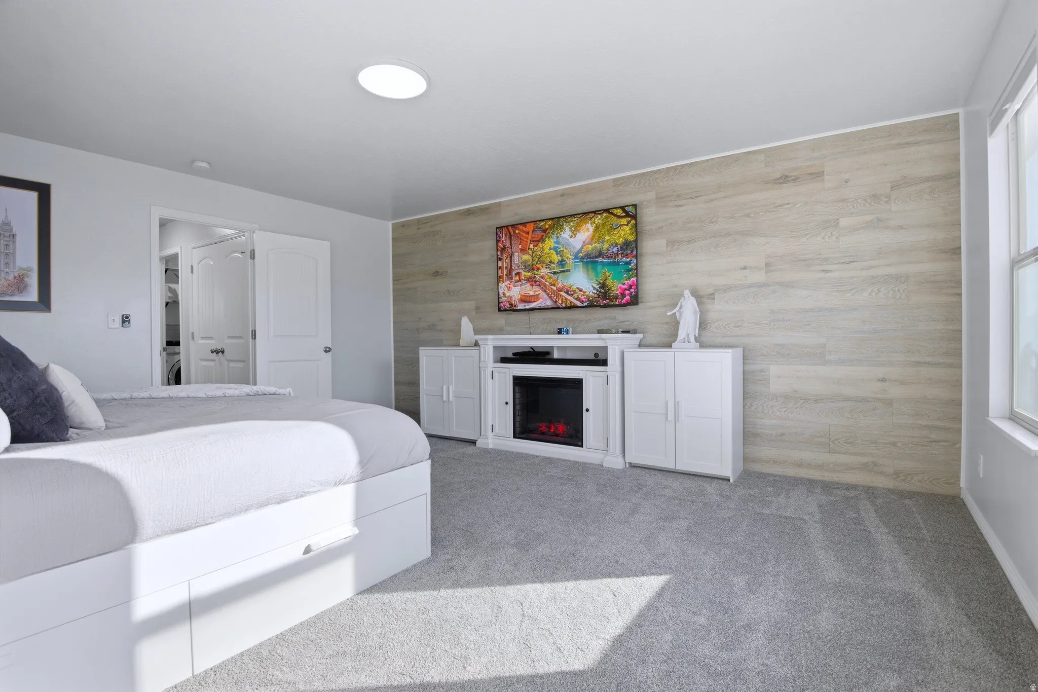 Bedroom featuring an accent wall with wood-finish paneling, a ceiling-mounted light fixture, a large window, light gray carpeting, and a double-door closet entry