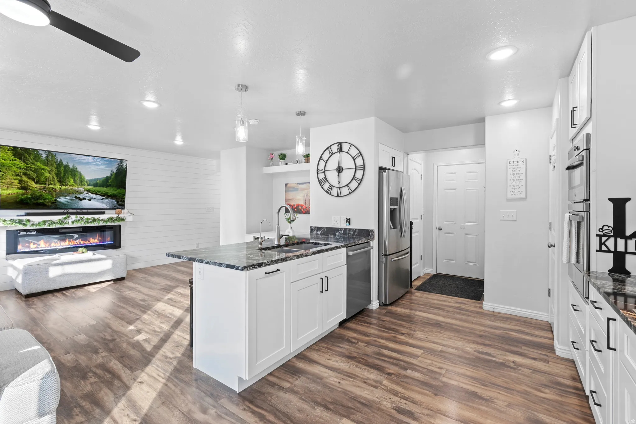 Modern kitchen featuring an island with a sink, stainless steel appliances, white cabinetry, and wood-finish flooring throughout