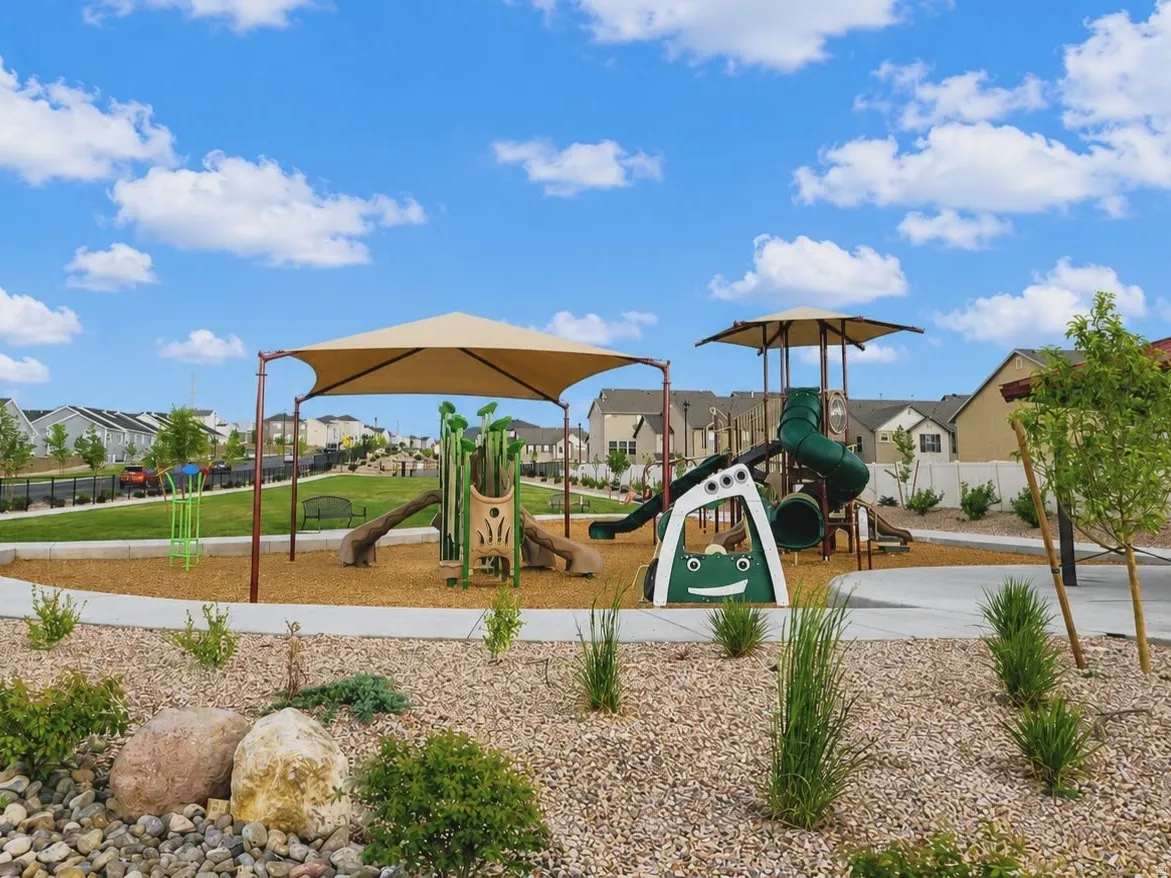 Community playground featuring multiple slides and climbing structures, shaded areas, and a concrete pathway