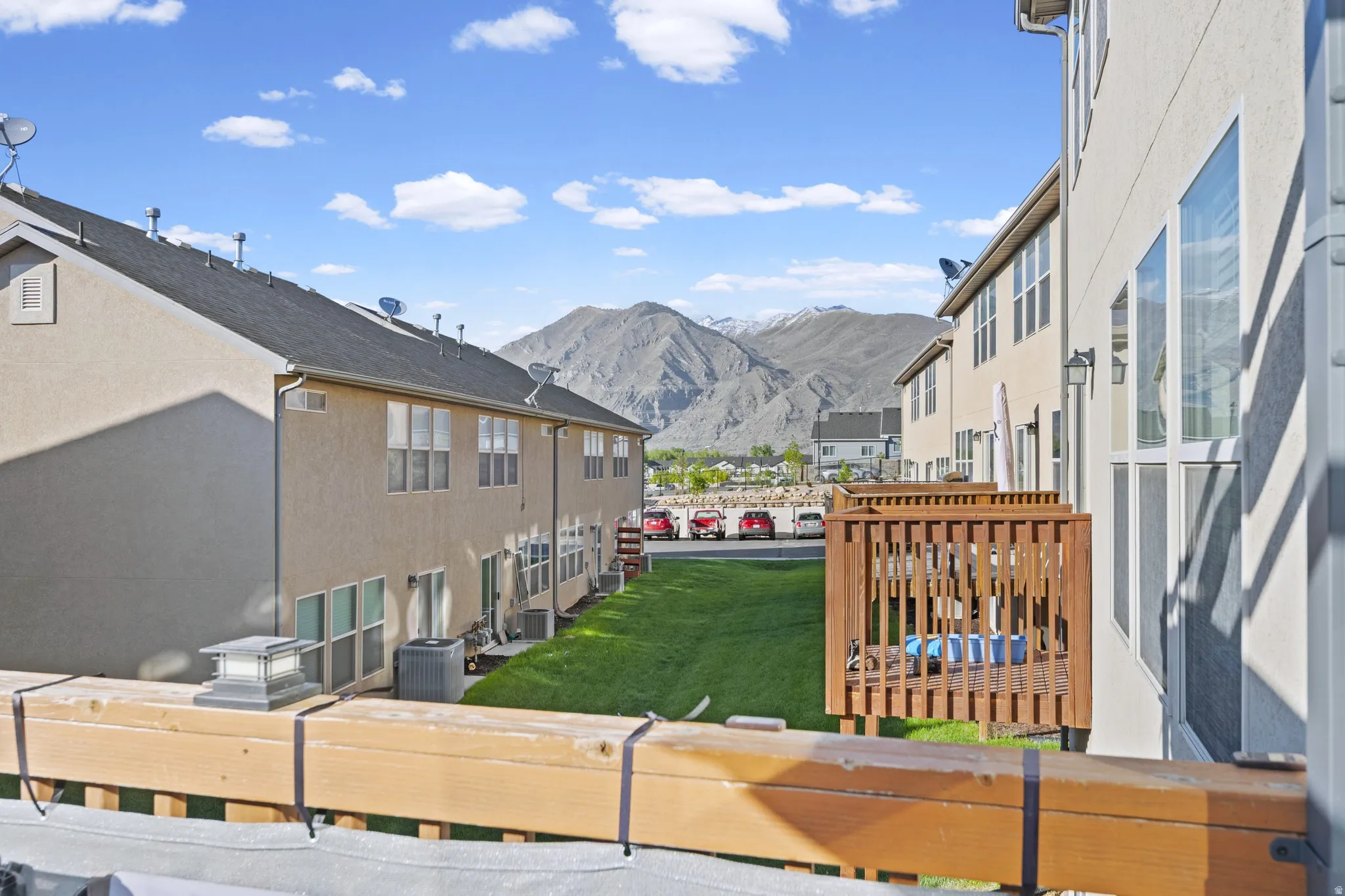 Property exterior featuring a private deck with natural wood railing, a green lawn, and mountain scenery