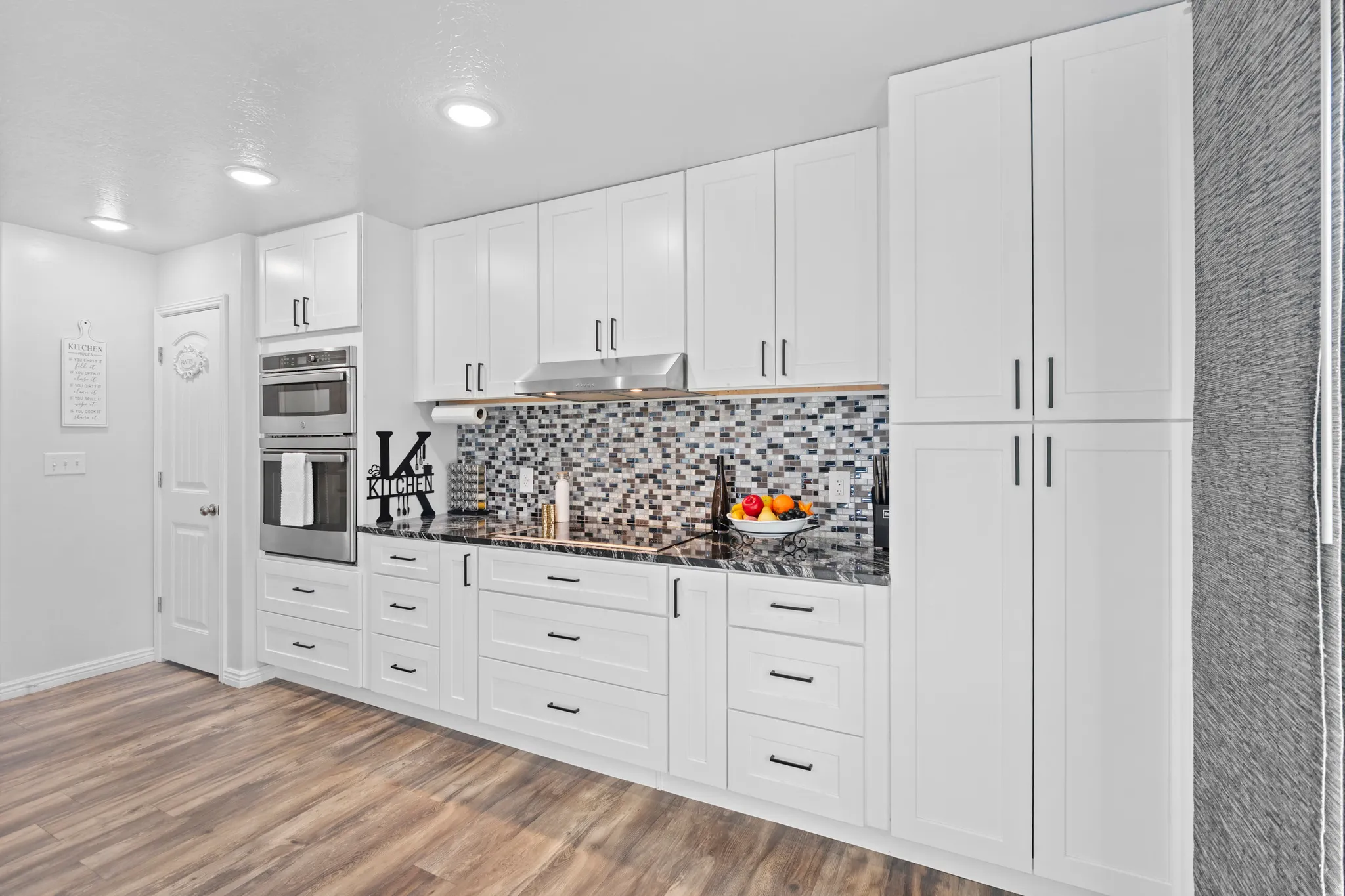 Modern kitchen featuring white shaker cabinetry with black hardware, black stone countertops, and a mosaic tile backsplash