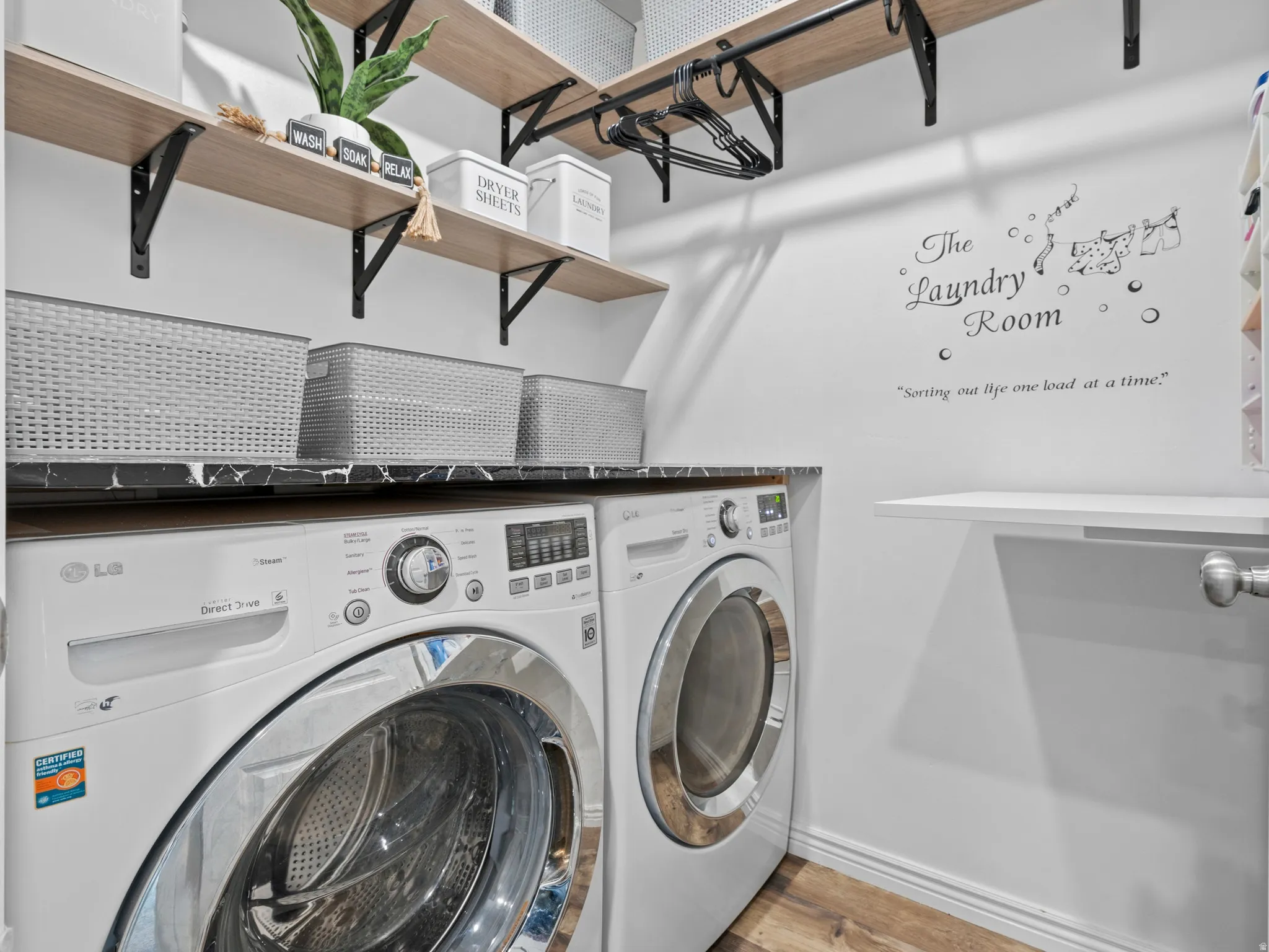 Dedicated laundry area featuring a dark countertop, upper wood-finish shelving with black brackets, and wood-finish flooring