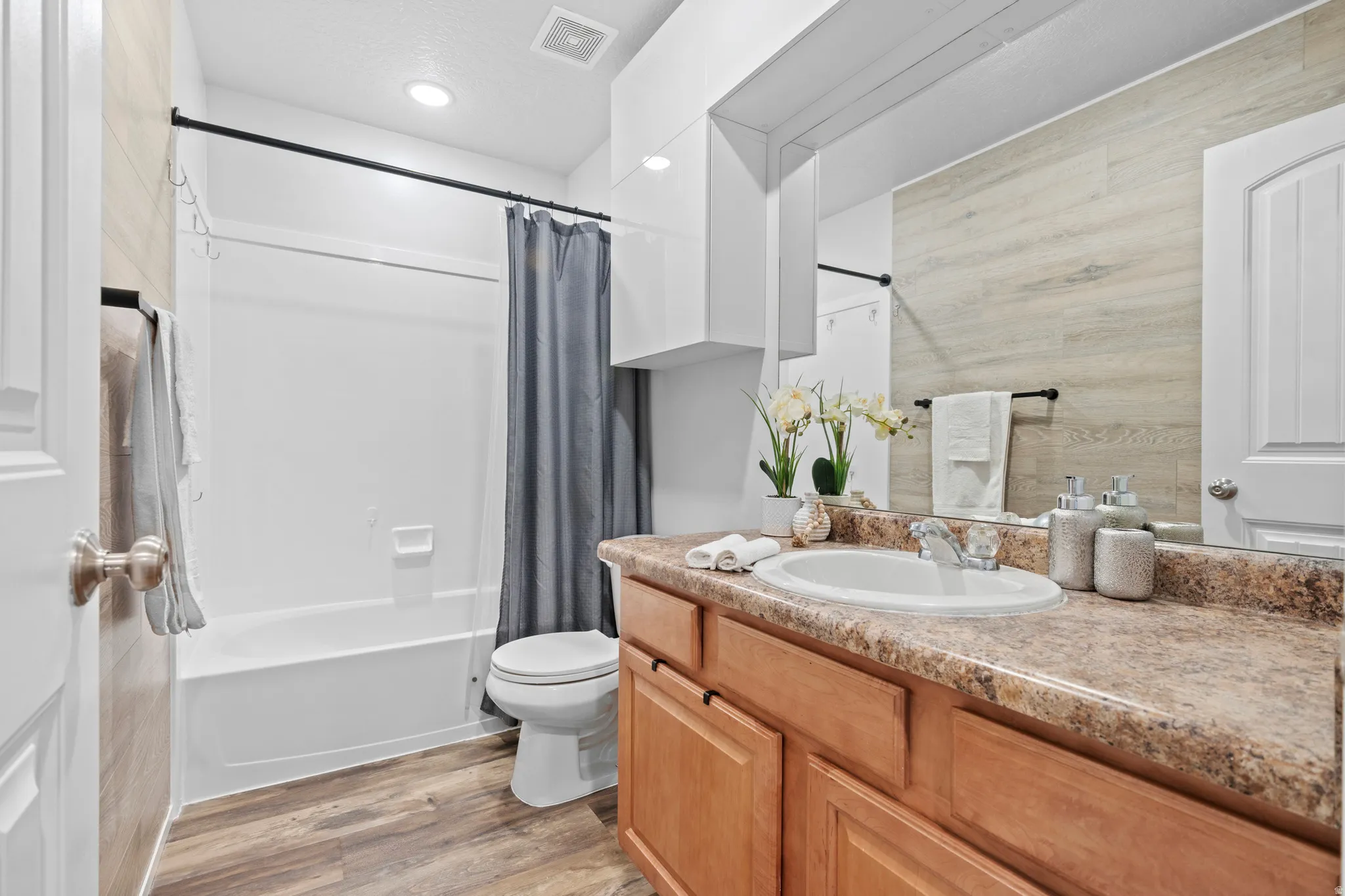 Bathroom featuring a single vanity with a laminate countertop, wood-finish flooring, a combination tub and shower, and a built-in medicine cabinet