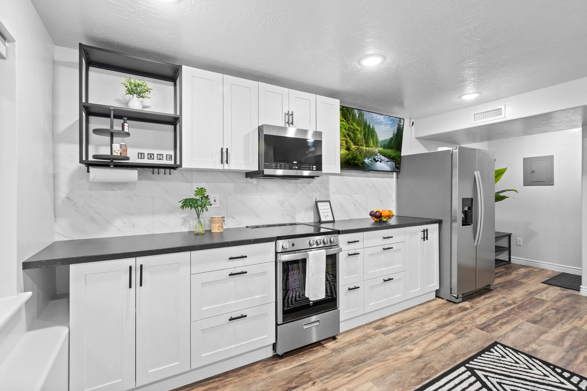 Modern kitchen featuring white shaker cabinetry, dark countertops, a marble-patterned backsplash, stainless steel appliances, and wood-finish flooring