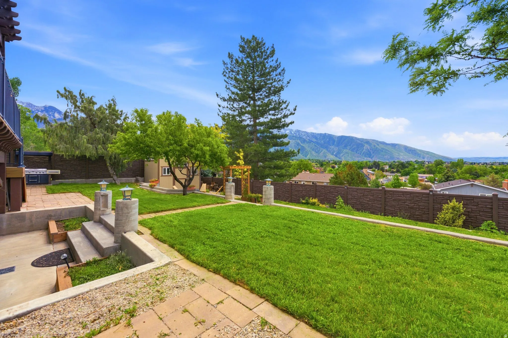 Tiered backyard featuring a manicured lawn, established trees, and a mountain backdrop