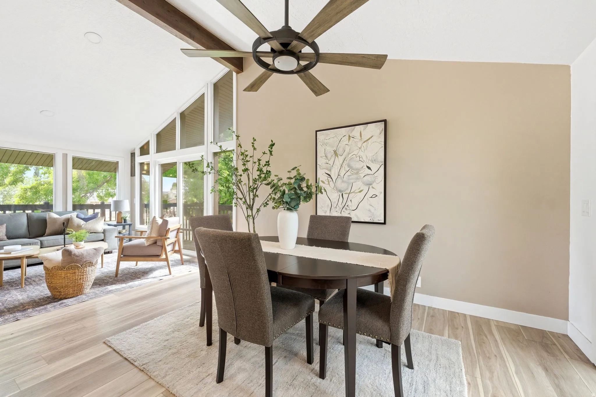Open-concept living and dining area featuring vaulted ceilings with exposed wood beams, a modern ceiling fan, and light wood-finish flooring