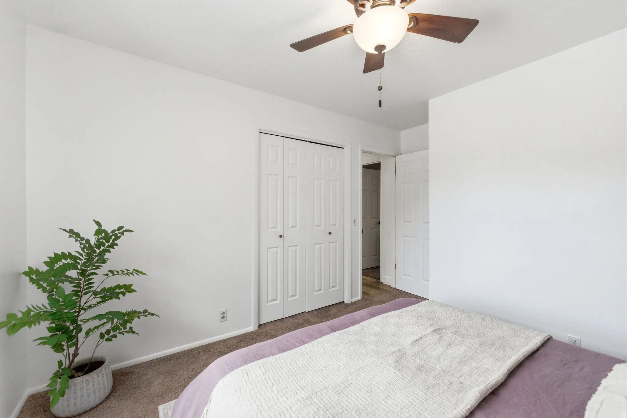 Bedroom featuring white walls, textured carpeting, a ceiling fan with integrated lighting, and bi-fold closet doors