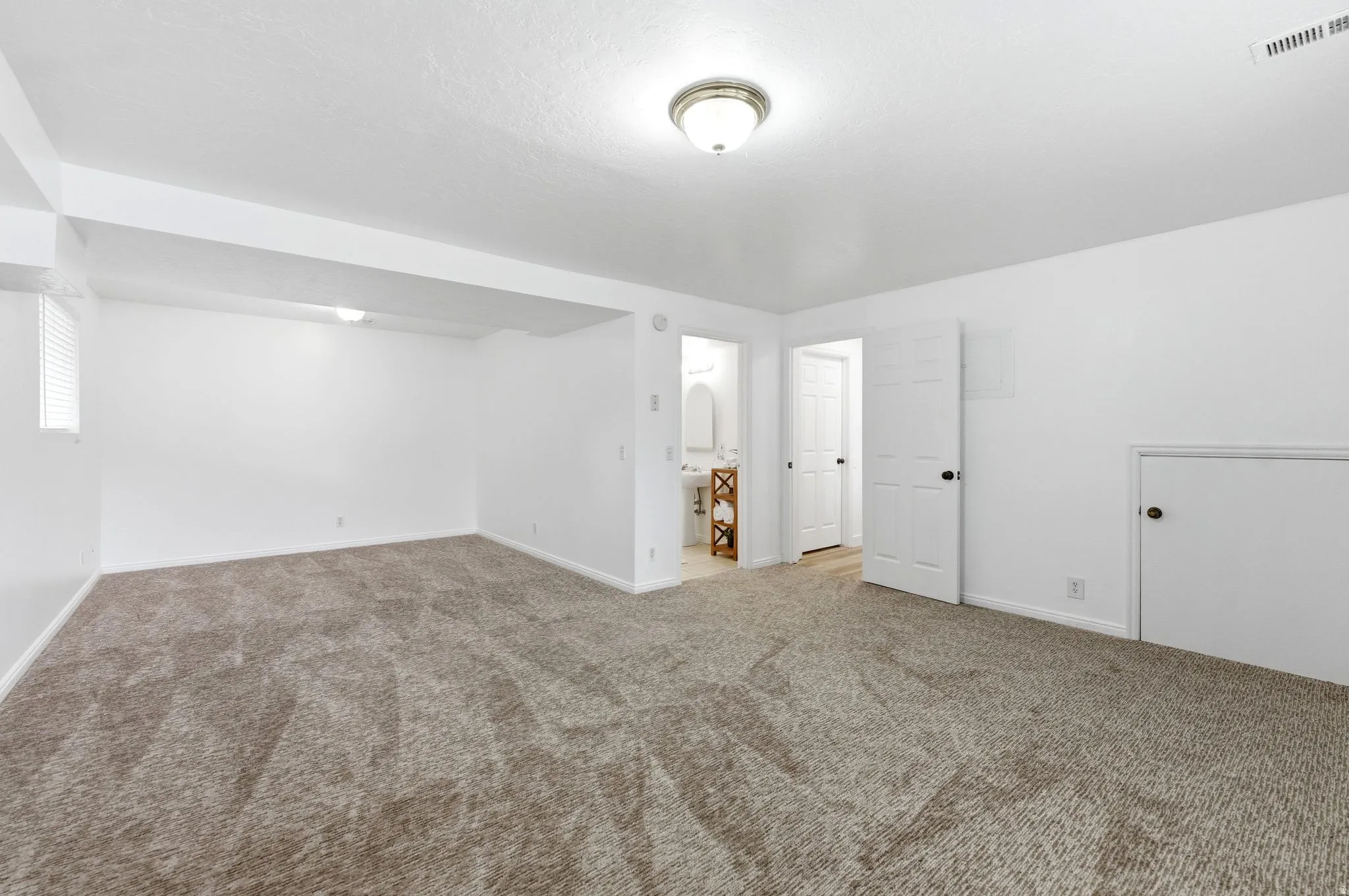 Spacious carpeted room featuring a ceiling-mounted light fixture, white walls, and a window with horizontal blinds