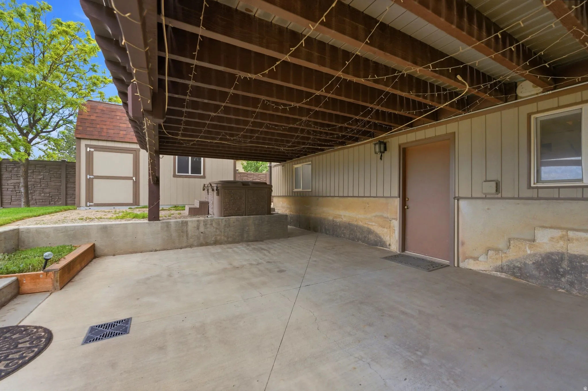 Covered concrete patio with exposed wood joist ceiling, providing an outdoor living area with hot tub
