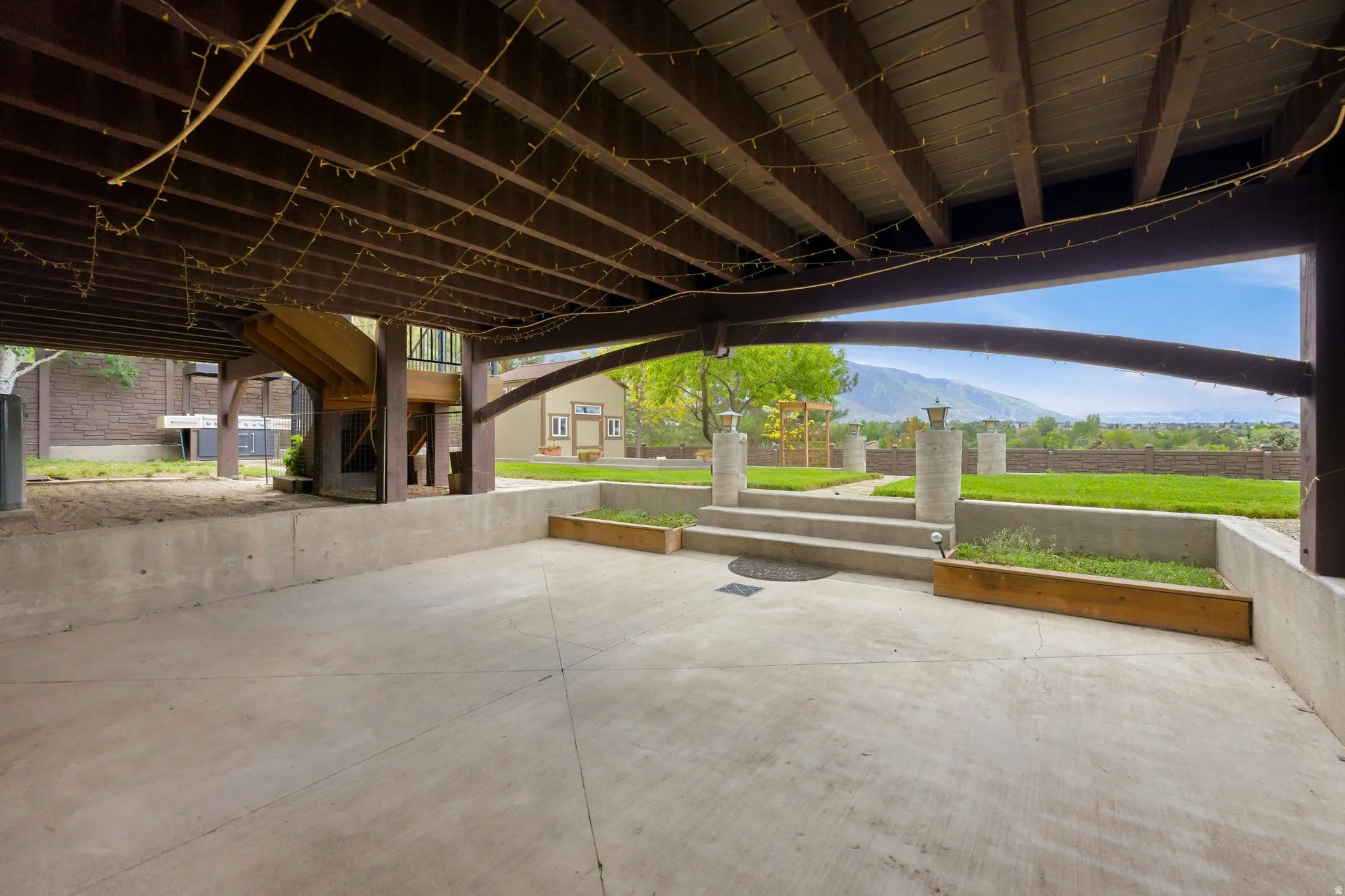 Covered concrete patio space featuring a spiral staircase, built-in planters, and concrete steps leading to a manicured lawn