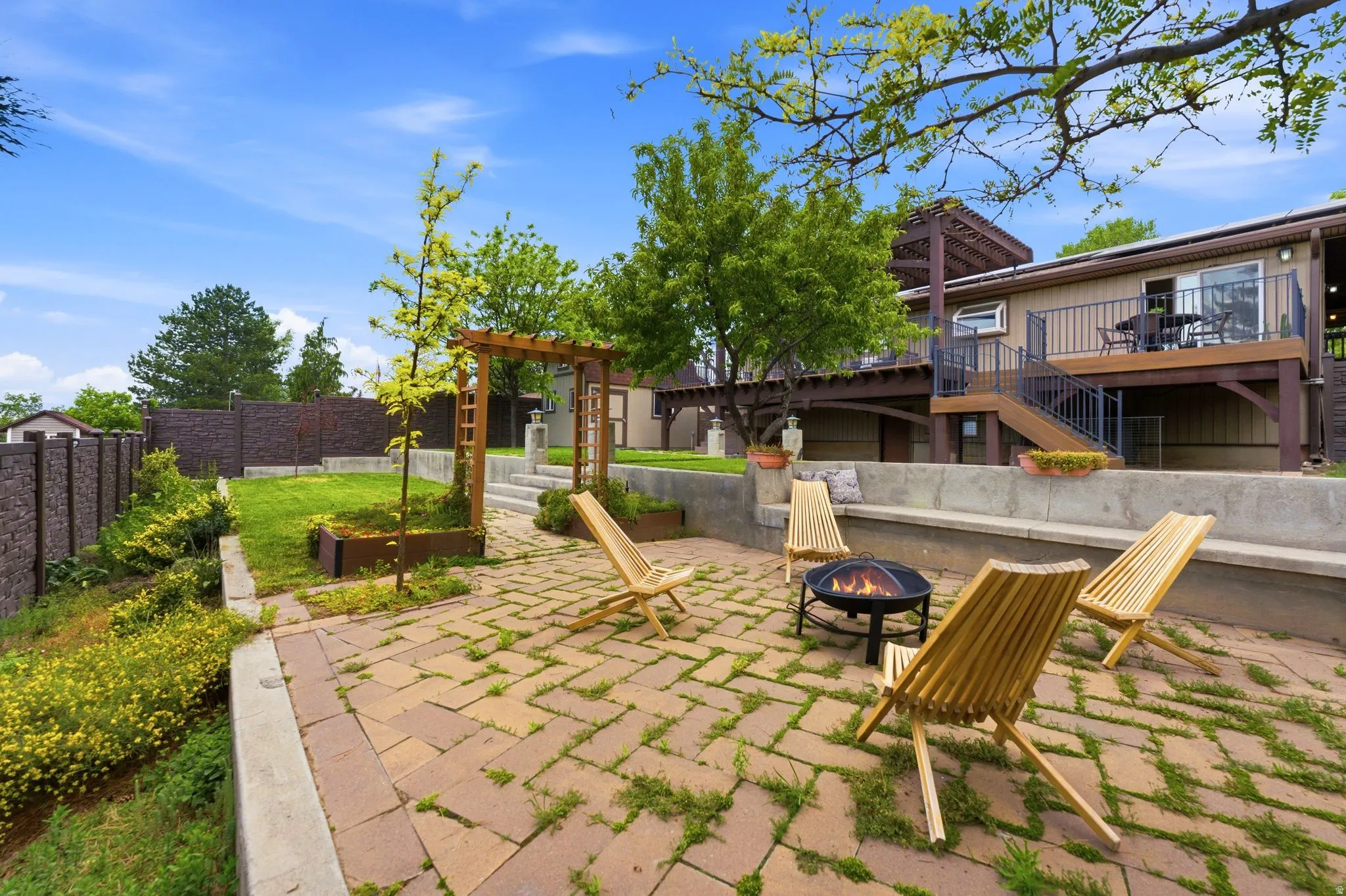 Multi-level outdoor living space featuring a paver patio with a built-in fire pit, a concrete retaining wall, and a raised lawn area