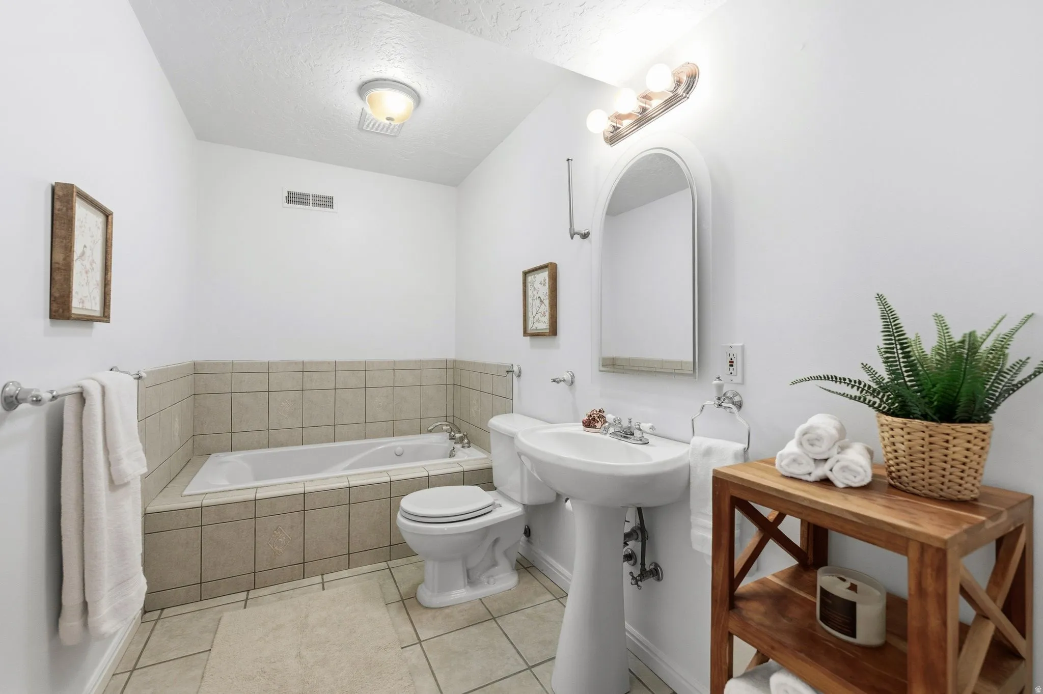 Bathroom featuring a pedestal sink, arched mirror, and a built-in tub with neutral tile surround