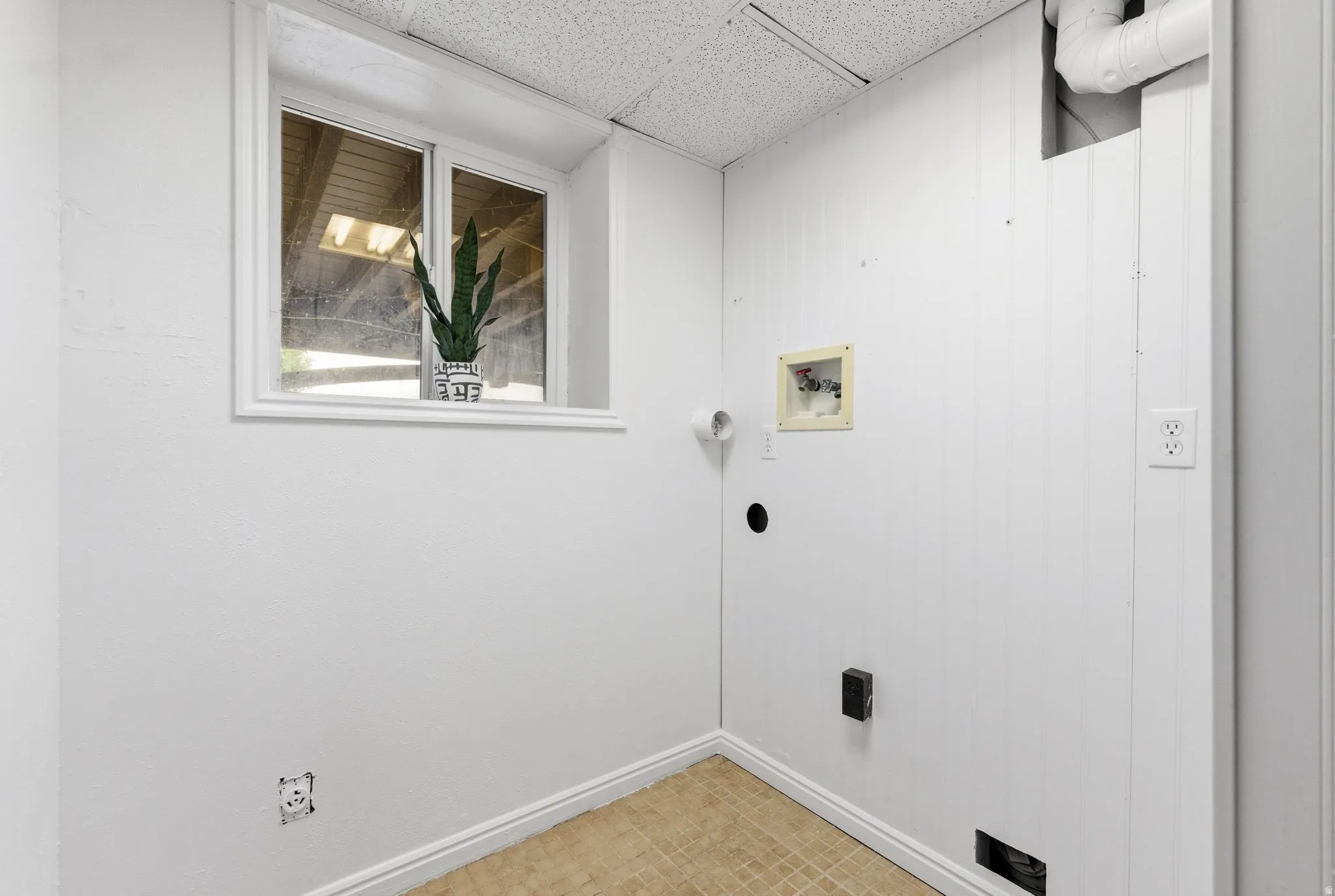 Dedicated utility space featuring a single window, white paneled walls, and a tiled ceiling