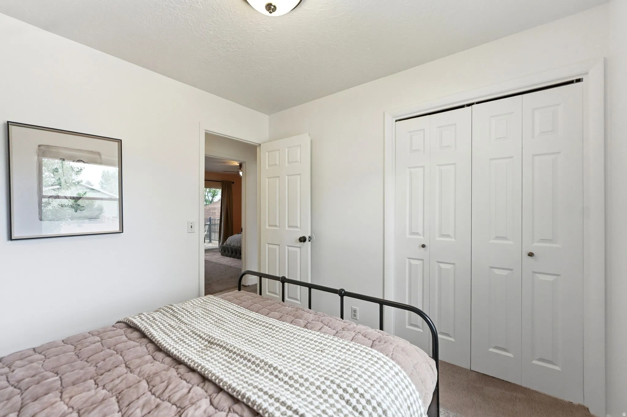 White interior walls, overhead flush mount light fixture, white bi-fold closet doors with black hardware, and an interior door with black hardware