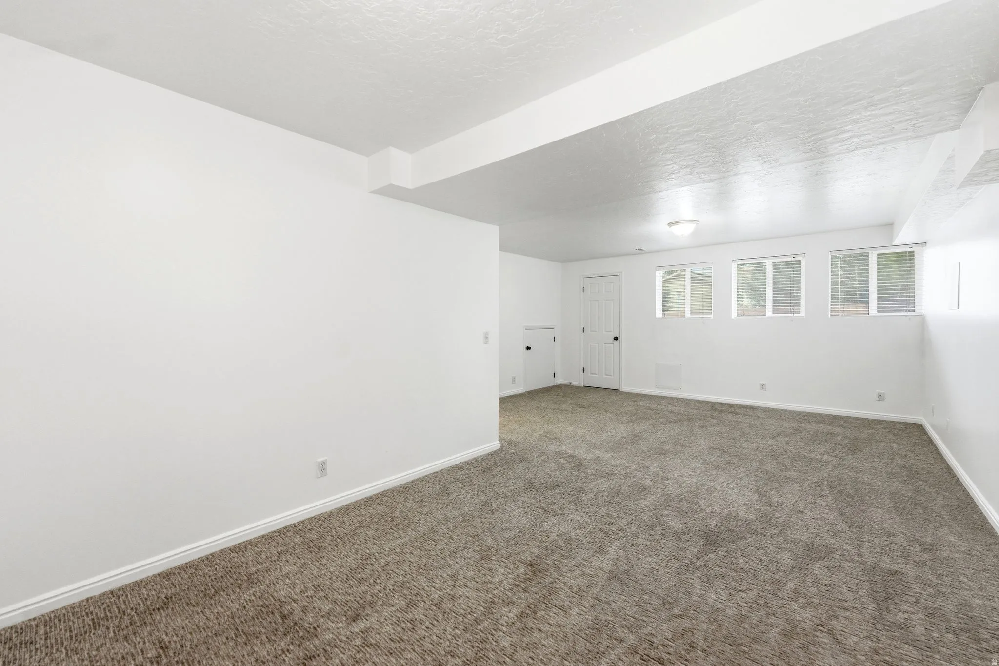 Spacious room featuring new carpeting, white baseboards, and multiple windows with blinds