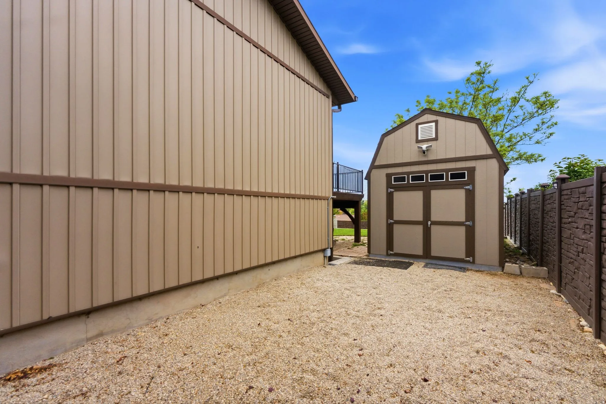 Gravel yard featuring a gambrel-roof shed with double doors and transom windows