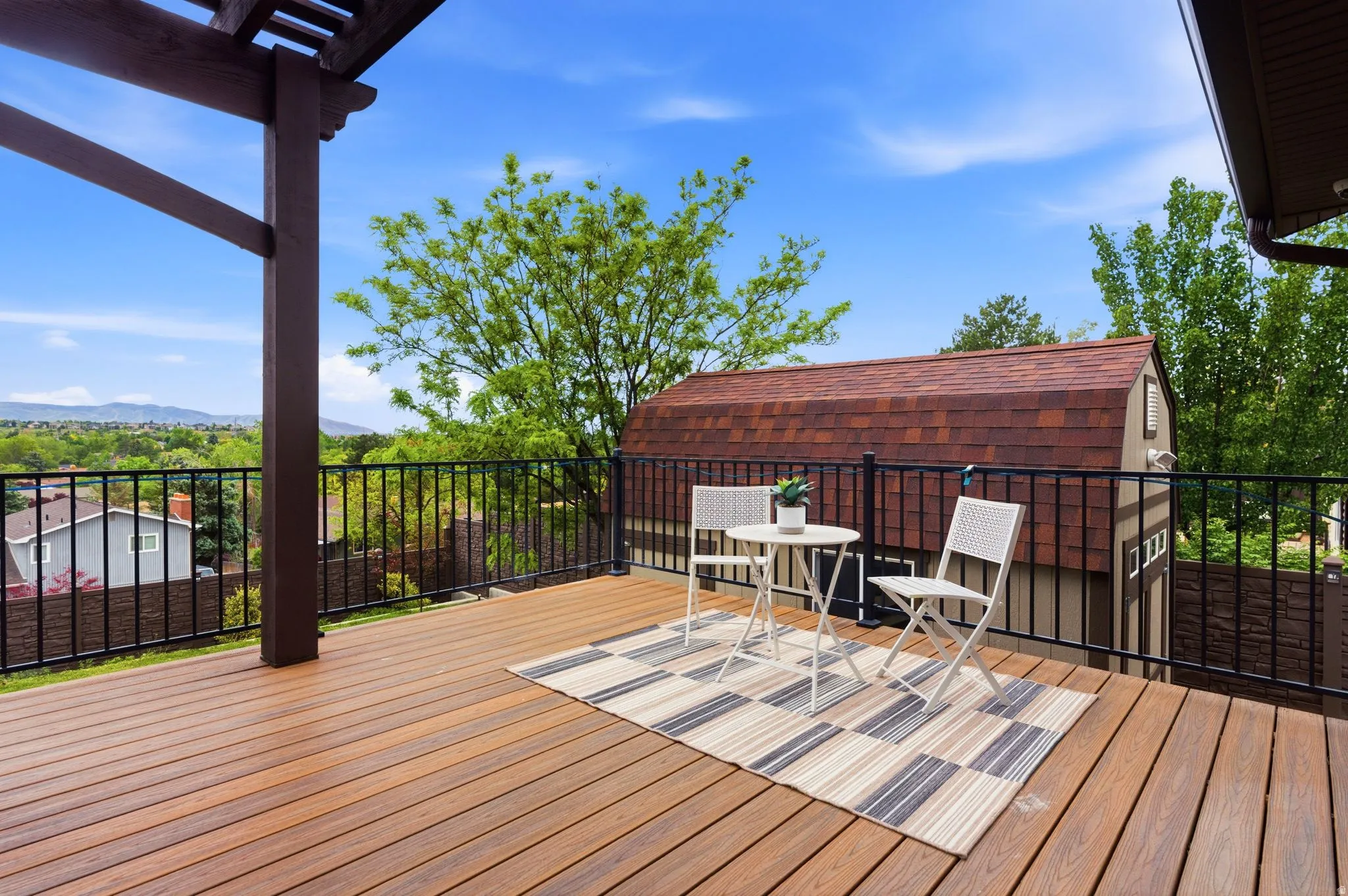 Expansive wood-finish deck with a pergola structure and black metal railings, featuring a detached shed with a shingle roof