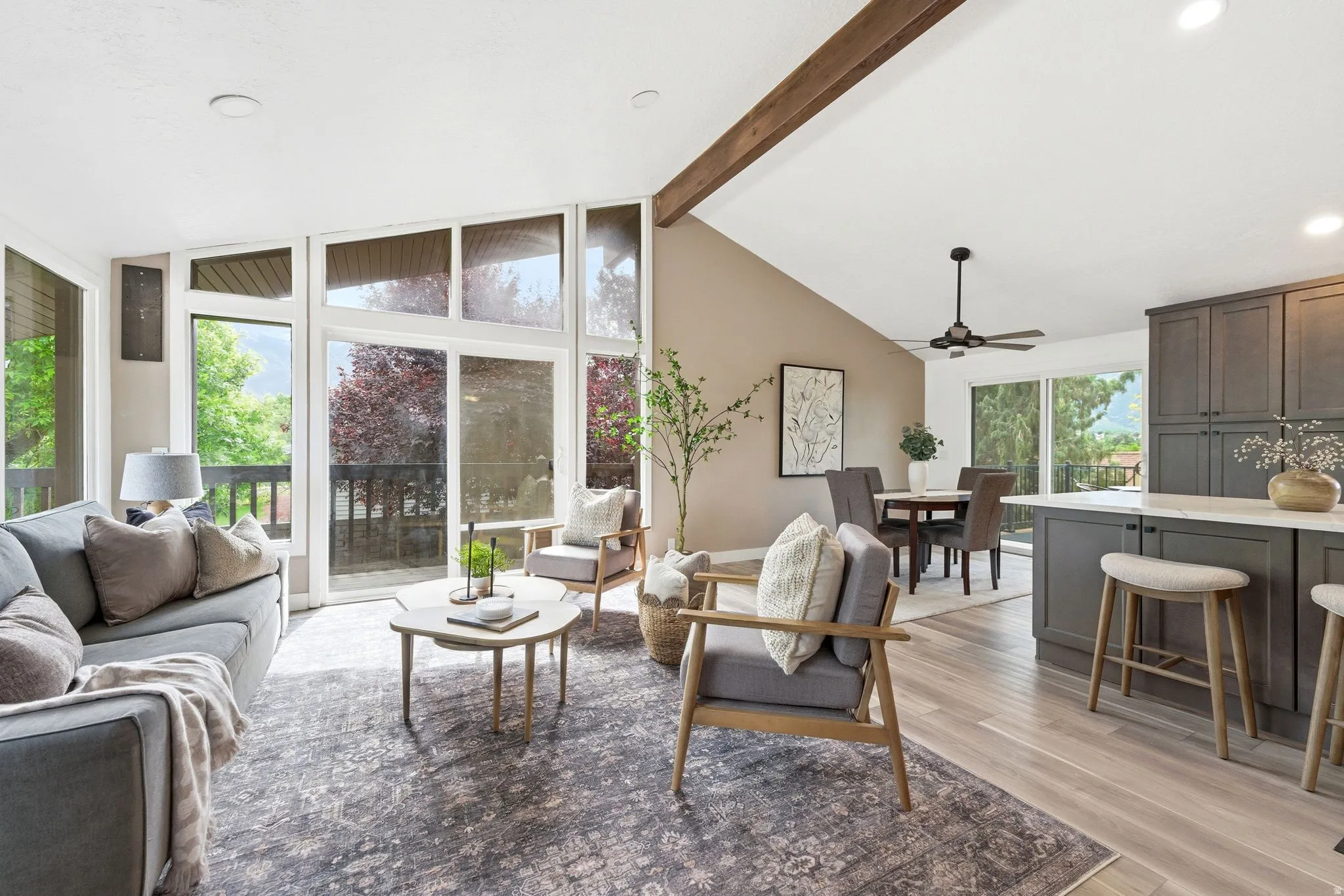 Vaulted ceiling living space featuring expansive windows, exposed wood beam, wood-finish flooring, recessed lighting, and a contemporary ceiling fan