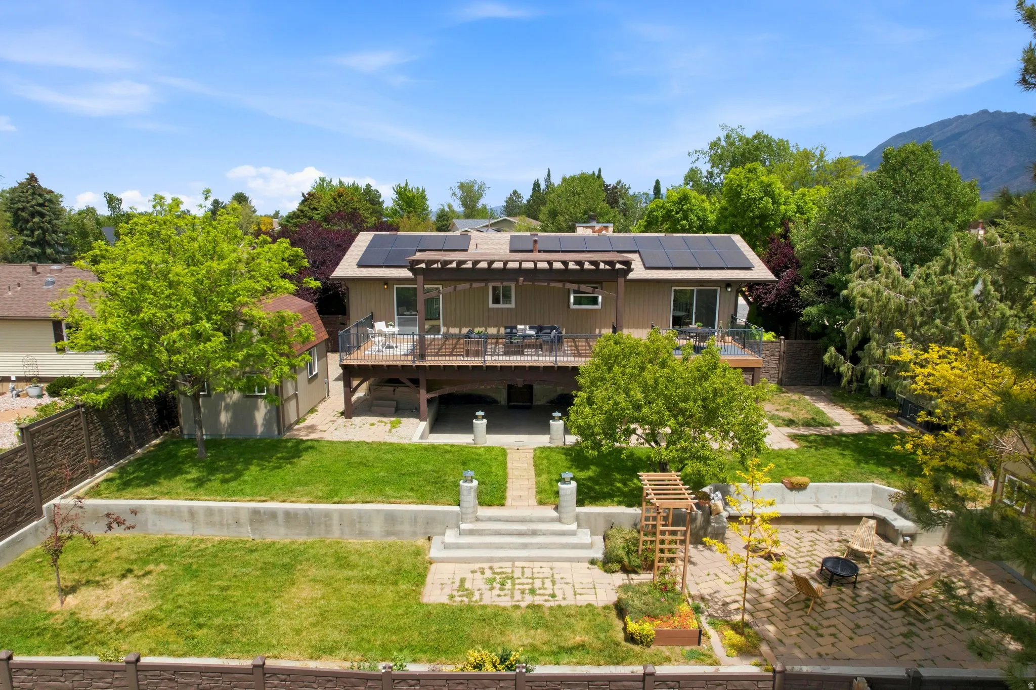 Multi-level backyard featuring a spacious wood deck, solar panels on the roof, a shed, and an outdoor patio with built-in bench seating and a fire pit