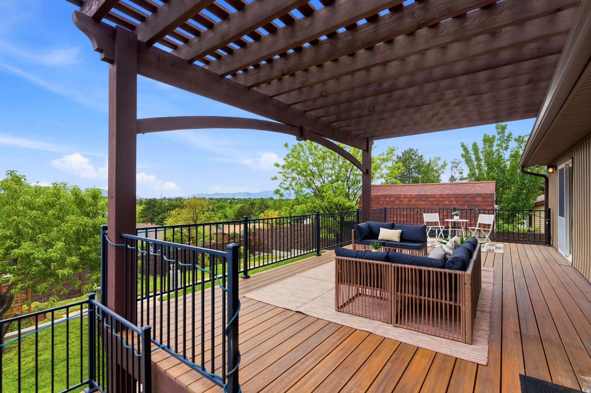 Expansive wood-finish deck with a large pergola structure, black metal railing, and distant mountain scenery