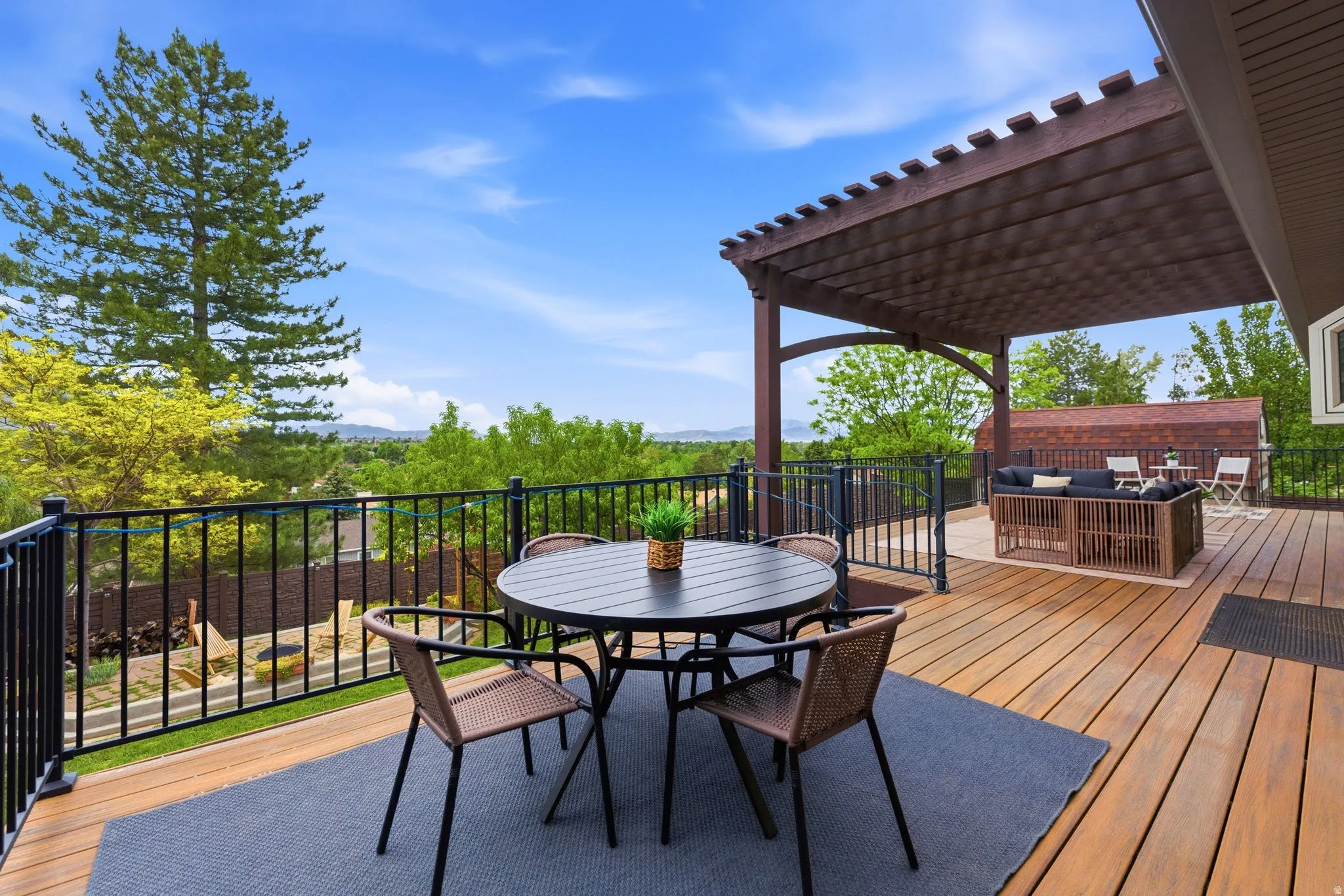 Expansive outdoor deck featuring composite wood-finish flooring, a dark brown pergola, and black metal railings