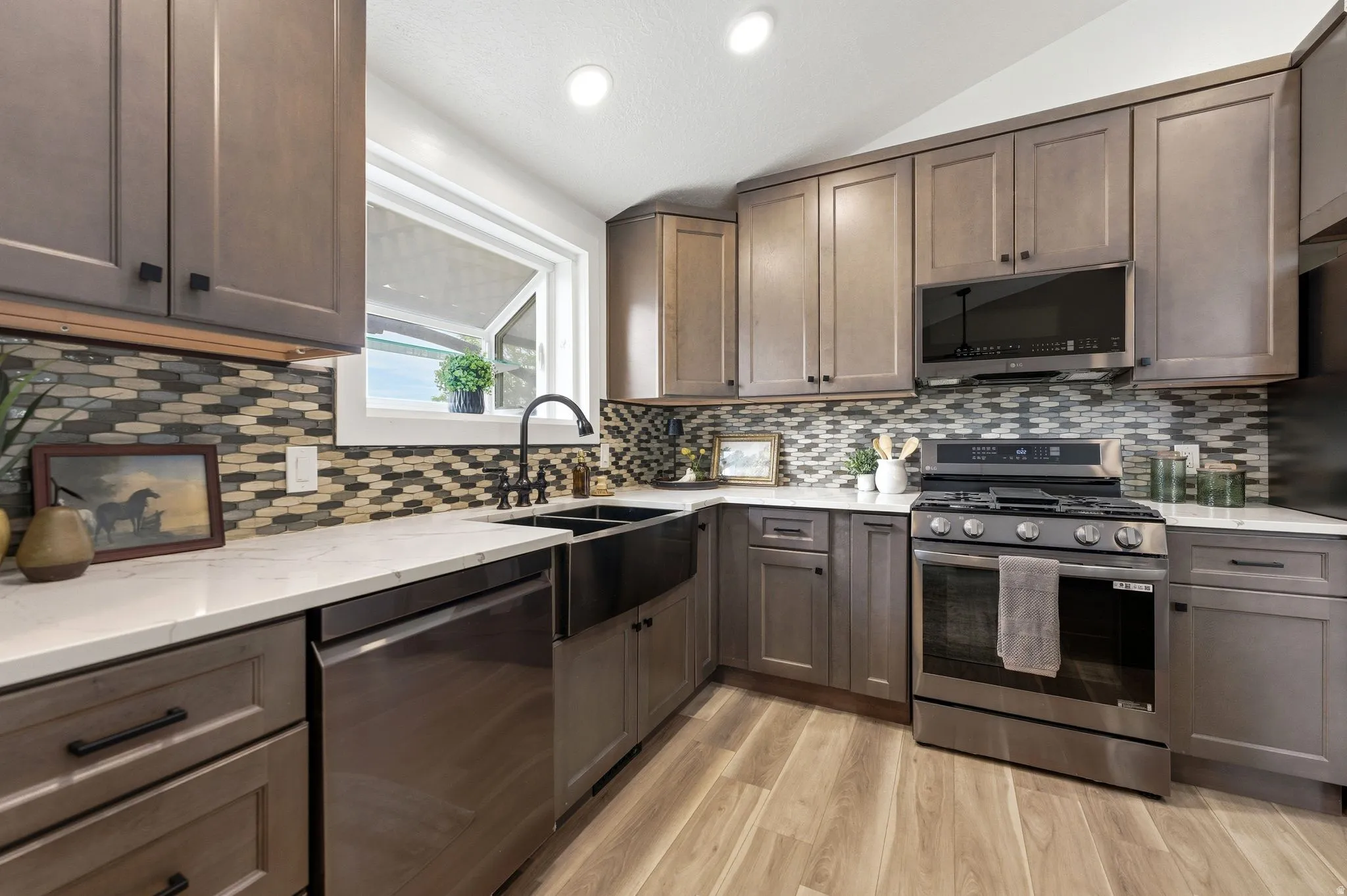 Kitchen featuring wood-finish cabinetry, stainless steel appliances including a range and dishwasher, and a multi-toned tile backsplash