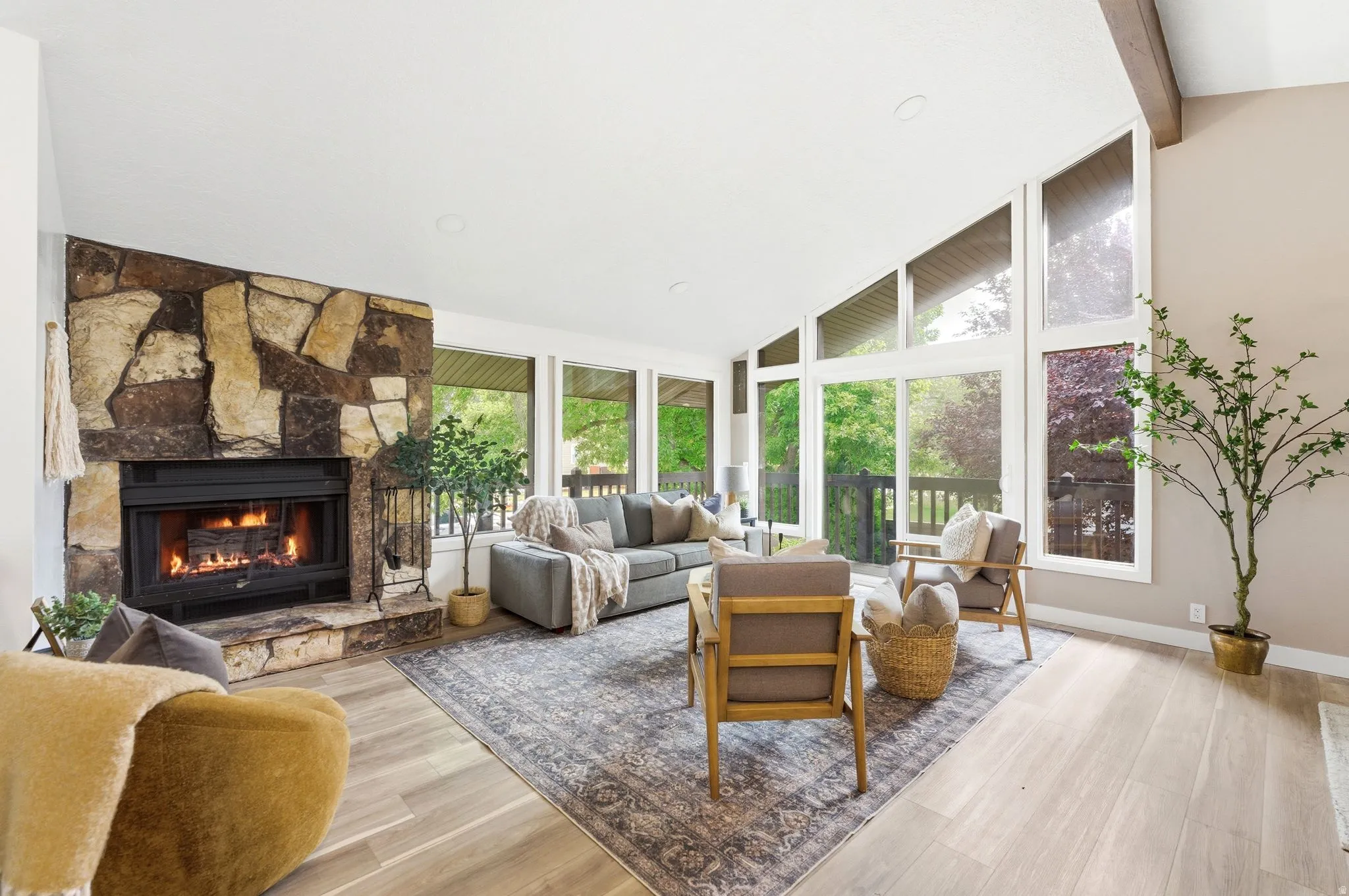 Spacious living area featuring an expansive stone fireplace, vaulted ceiling with exposed wood beam, and numerous large windows