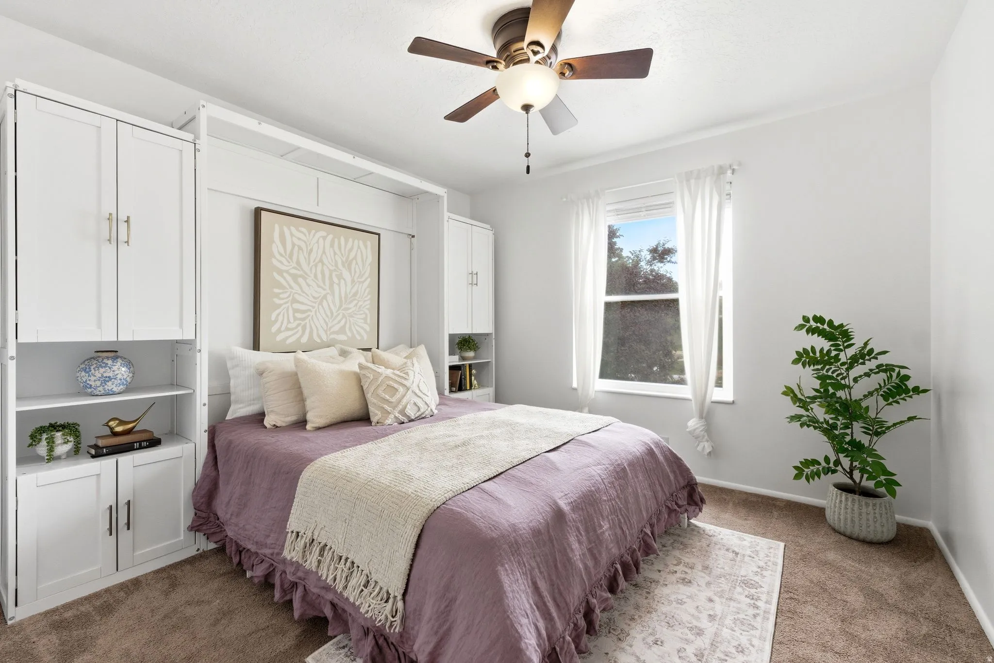Built-in white cabinetry with gold-finish hardware, brown ceiling fan light fixture, carpet flooring, and a double-hung window