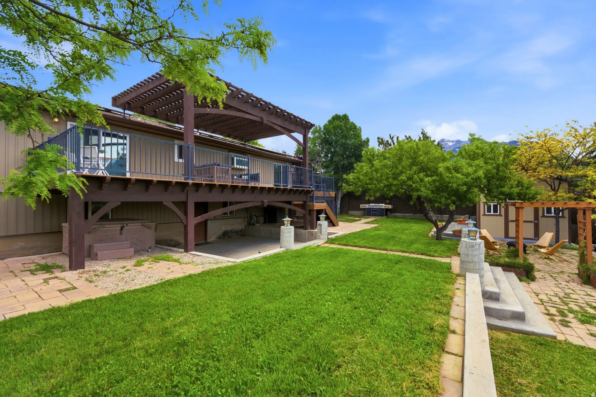 Expansive backyard featuring a large elevated deck with a pergola, a manicured lawn, a built-in hot tub, and a separate patio area with an additional pergola structure