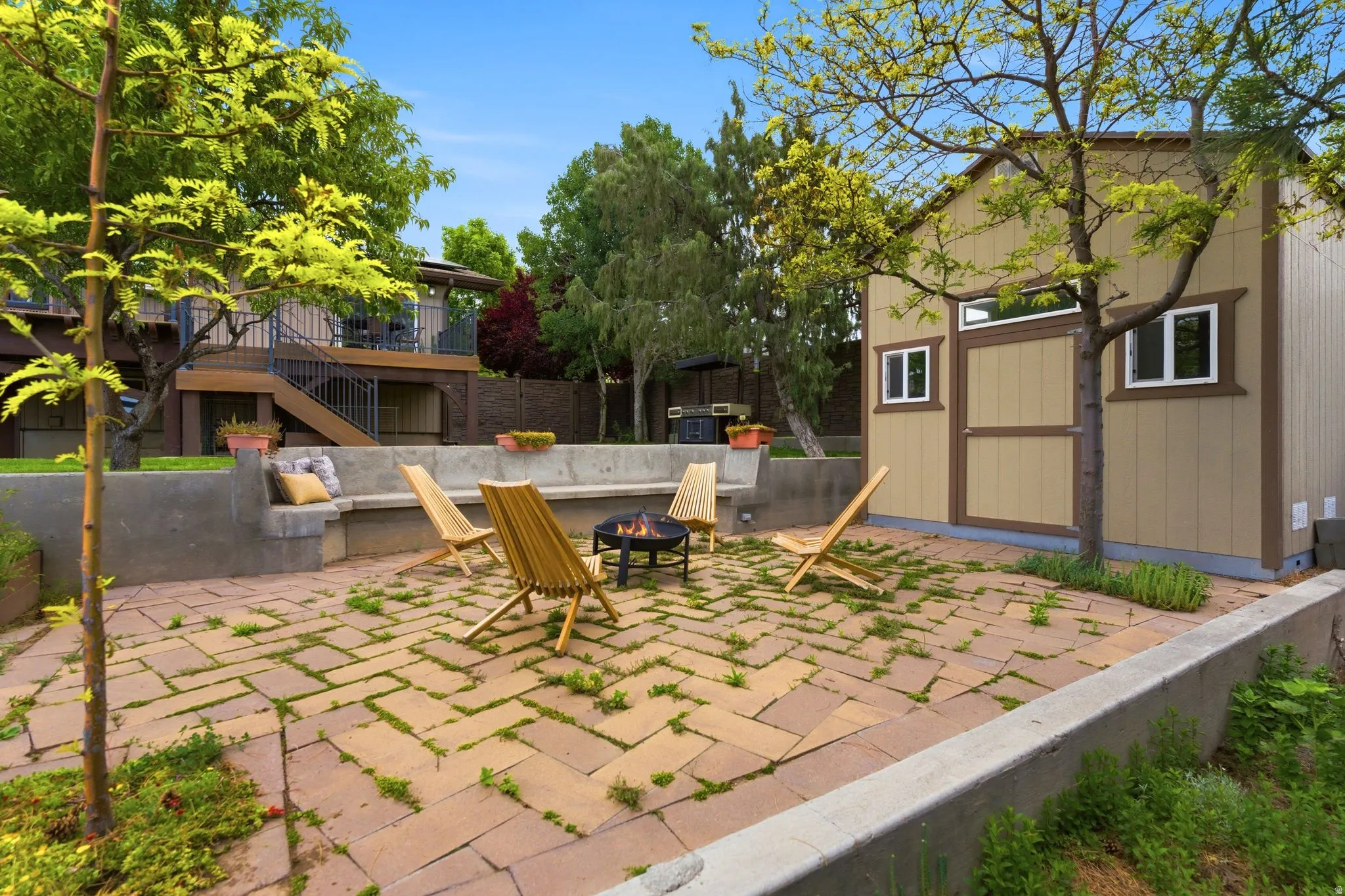 Paved patio area featuring a built-in concrete bench, a fire pit, and a detached auxiliary structure with a pitched roof